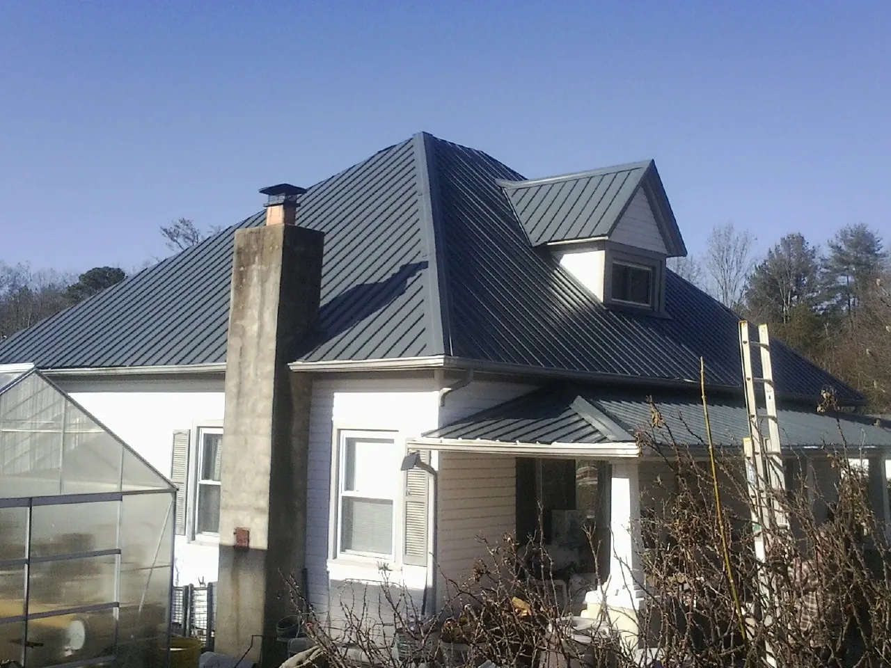 Dark blue standing seam metal roof on a white farmhouse with dormer — Slate & Tile Roof Repair by Roofing Brothers in Ponce De Leon