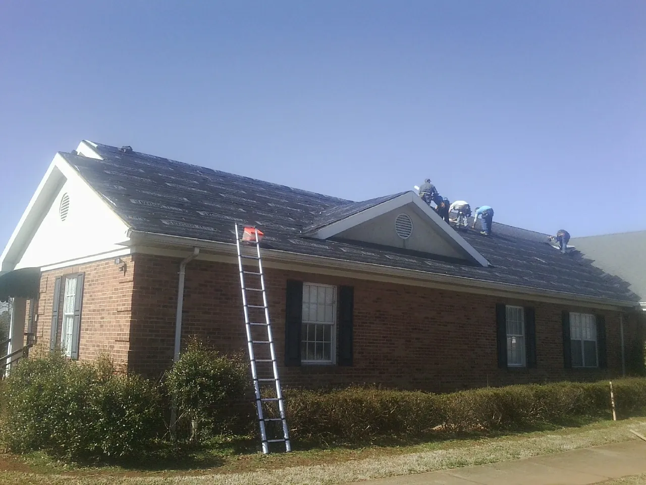 Crew tearing shingles off a brick ranch roof with a ladder set — Emergency Roof Repair work by our crew in Ponce De Leon