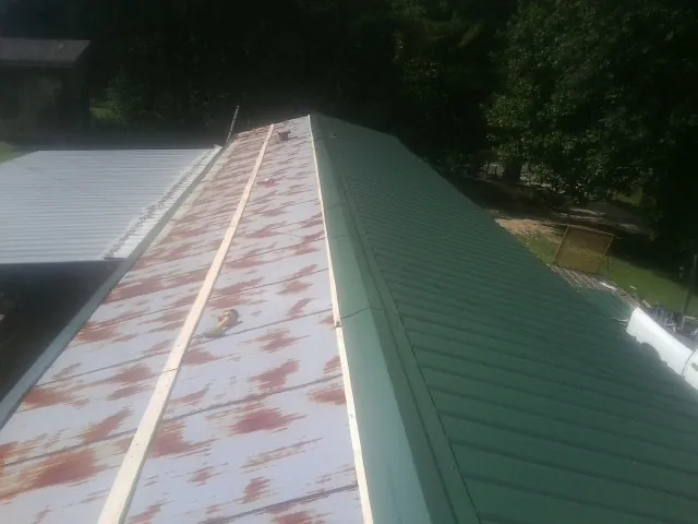 Old rusted panels beside newly installed green metal roofing — Wind Damage Roof Repair by Roofing Brothers in Ponce De Leon