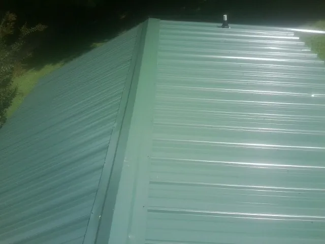 New green metal panels meeting at the ridge of a roof — Flat Roof Repair work by our crew in Ponce De Leon