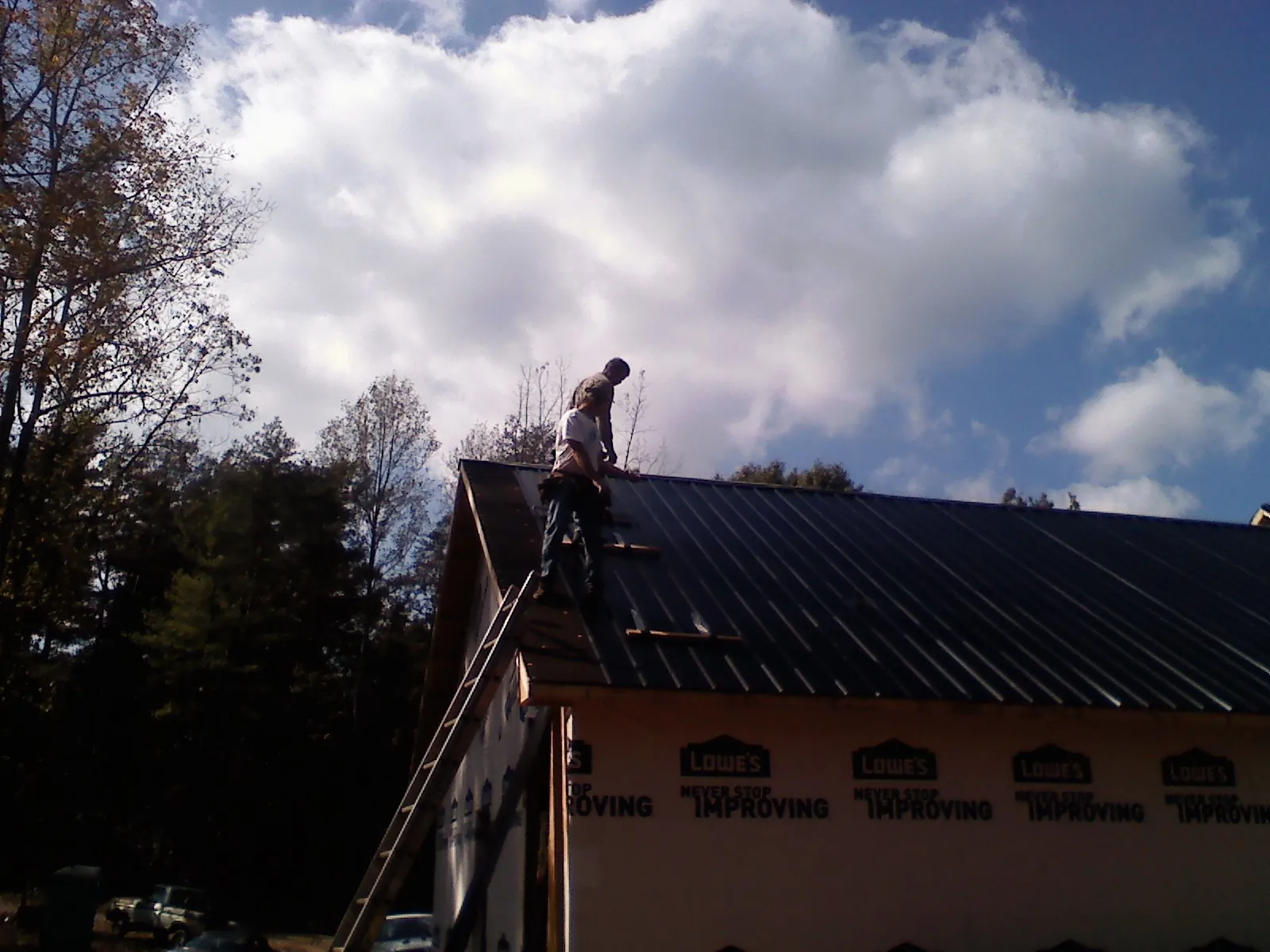 Roofer fastening dark metal panels high against a cloudy sky, from a Roof Inspection job in Ponce De Leon