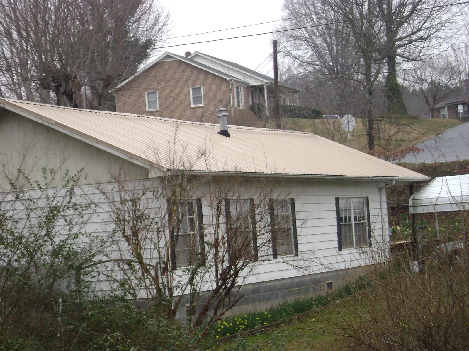 Tan metal roof on a white sided house set into a hillside — Commercial Roofing by Roofing Brothers in Ponce De Leon