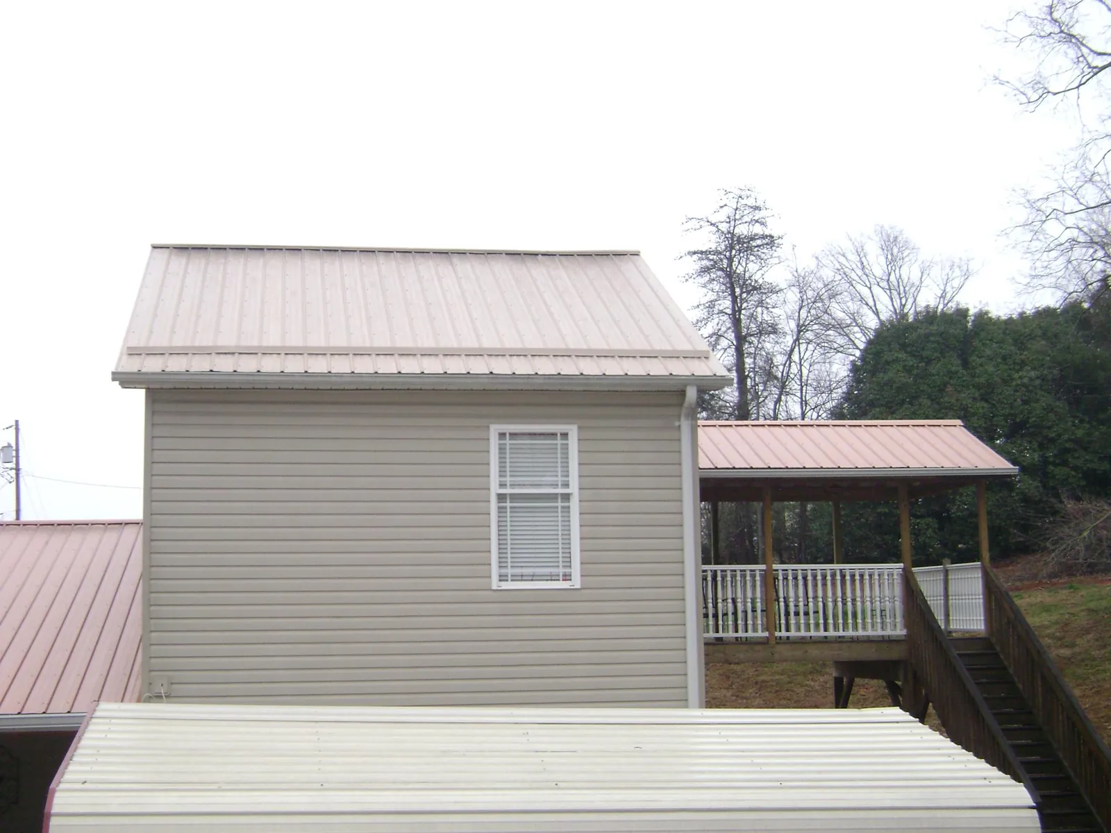 Tan metal roofs on a two story addition and attached porch, from a Roof Replacement job in Ponce De Leon